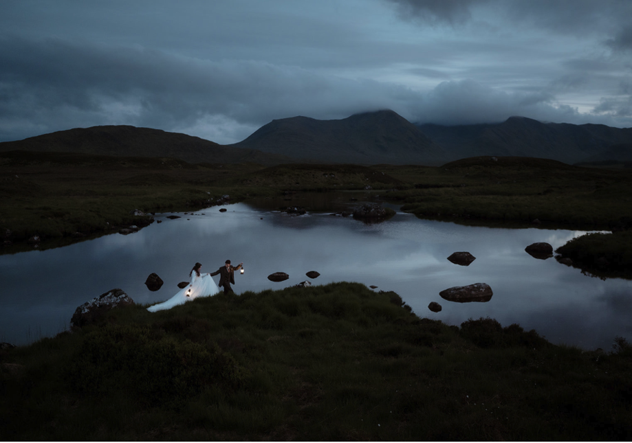 Eloping couple walking through the moors holding lanterns in Glencoe, Scotland